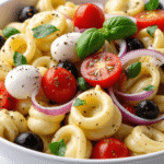 Close-up of tortellini salad with tomatoes, mozzarella balls, olives, onions, basil, and cracked black pepper.