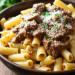A hearty bowl of rigatoni pasta topped with tender beef chunks coated in creamy garlic butter sauce, sprinkled with Parmesan and parsley.