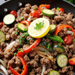 Ground beef stir fry with zucchini, bell peppers, onions, and cherry tomatoes, topped with a slice of lemon and fresh parsley.
