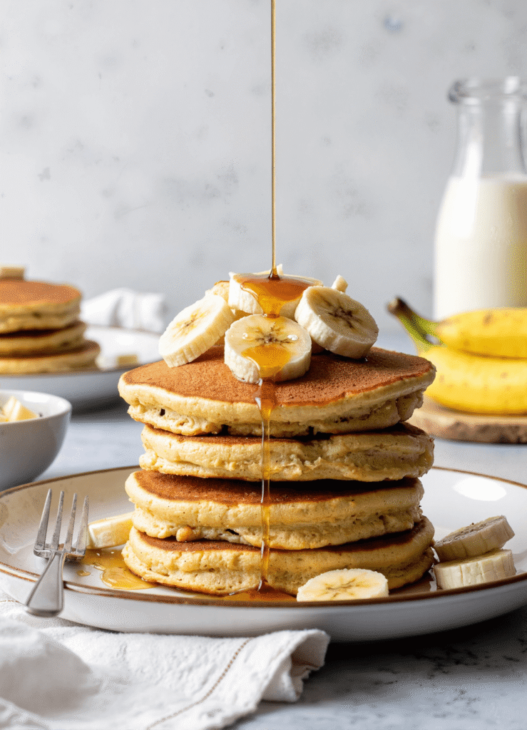 Stack of fluffy banana cottage cheese pancakes topped with fresh banana slices and maple syrup drizzle.
