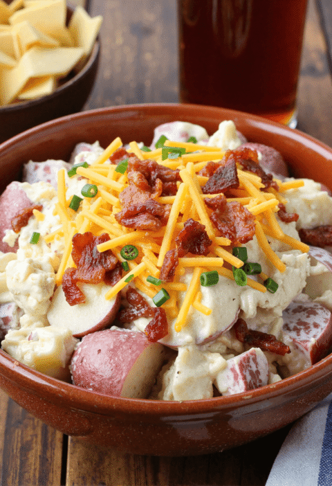 Creamy steakhouse potato salad with red potatoes, bacon, and shredded cheddar in a brown bowl.