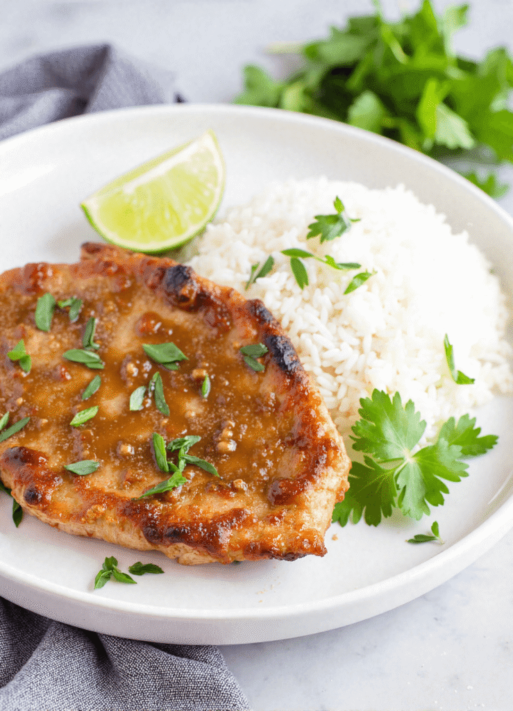 Golden-brown pork chop with ginger lime glaze and coconut rice on a white plate with lime wedge