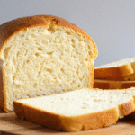 Sliced high-protein yogurt bread on a round wooden board with soft, airy texture and golden crust.