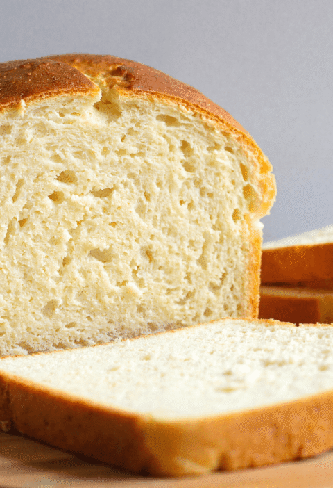 Sliced high-protein yogurt bread on a round wooden board with soft, airy texture and golden crust.