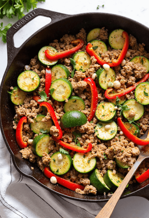 Close-up of one-pan turkey and zucchini skillet with sliced red bell peppers and white beans in a cast iron pan