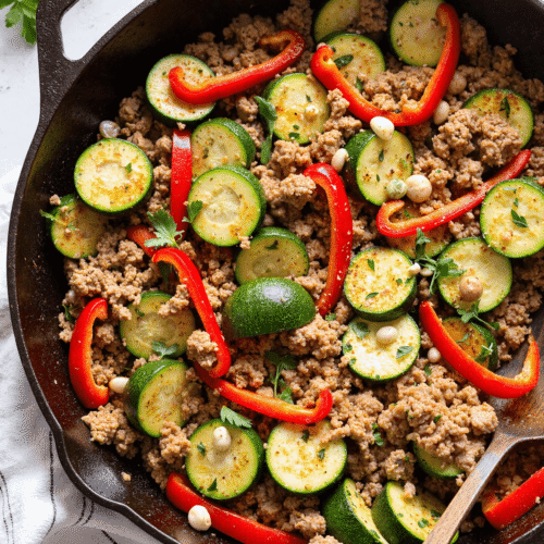 Close-up of one-pan turkey and zucchini skillet with sliced red bell peppers and white beans in a cast iron pan