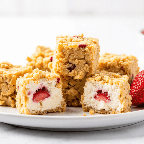 Strawberry cheesecake crunch bites with fresh strawberries on a white plate, showing creamy cheesecake filling and crunchy cookie coating.