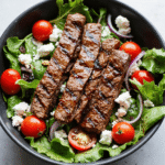 Grilled steak slices on a bed of fresh greens with cherry tomatoes, red onion, feta cheese, and balsamic vinaigrette.