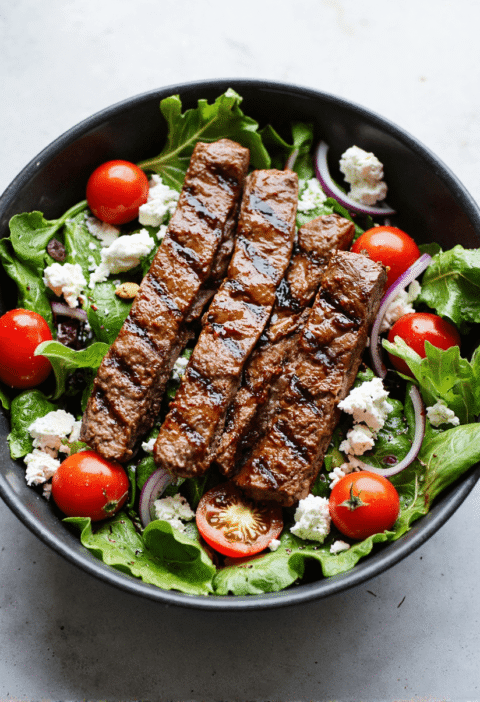 Grilled steak slices on a bed of fresh greens with cherry tomatoes, red onion, feta cheese, and balsamic vinaigrette.