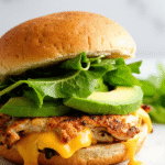 Chicken avocado melt sandwich with gooey cheddar cheese, fresh avocado slices, and crisp lettuce on a toasted bun.