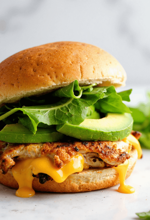 Chicken avocado melt sandwich with gooey cheddar cheese, fresh avocado slices, and crisp lettuce on a toasted bun.