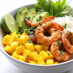 Grilled shrimp rice bowl with mango, avocado, fresh herbs, and lime in a white ceramic bowl.